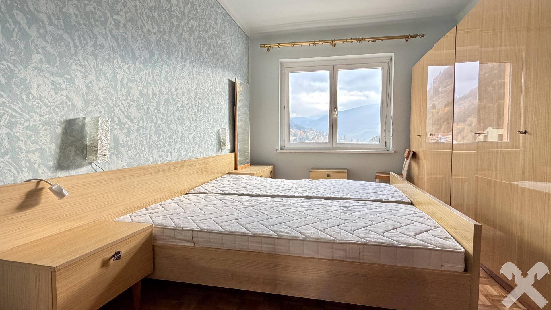 Schlafzimmer mit Doppelbett, Holzmöbeln und Tapete, bietet Bergblick durch das Fenster.