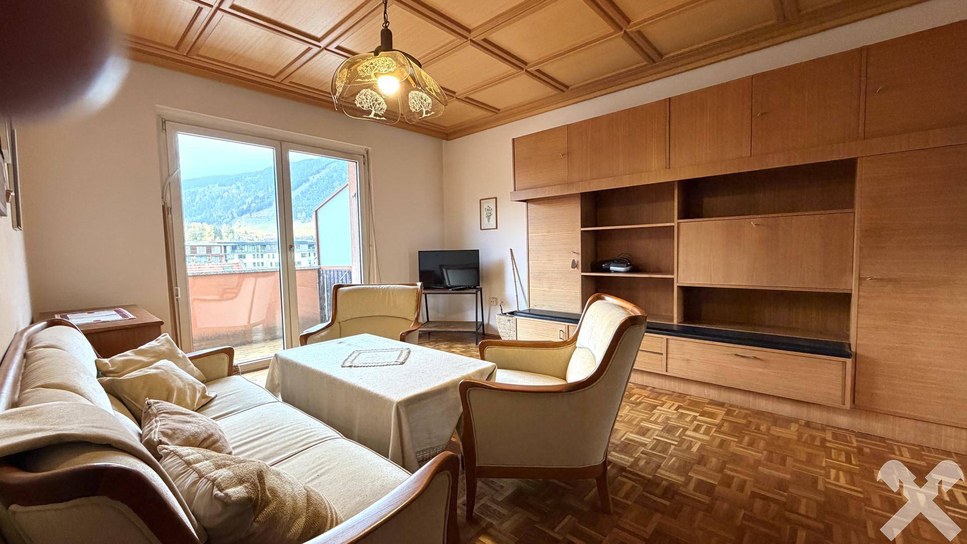 Gemütliches Wohnzimmer mit Holzdecke, Parkettboden und Zugang zu einem Balkon.