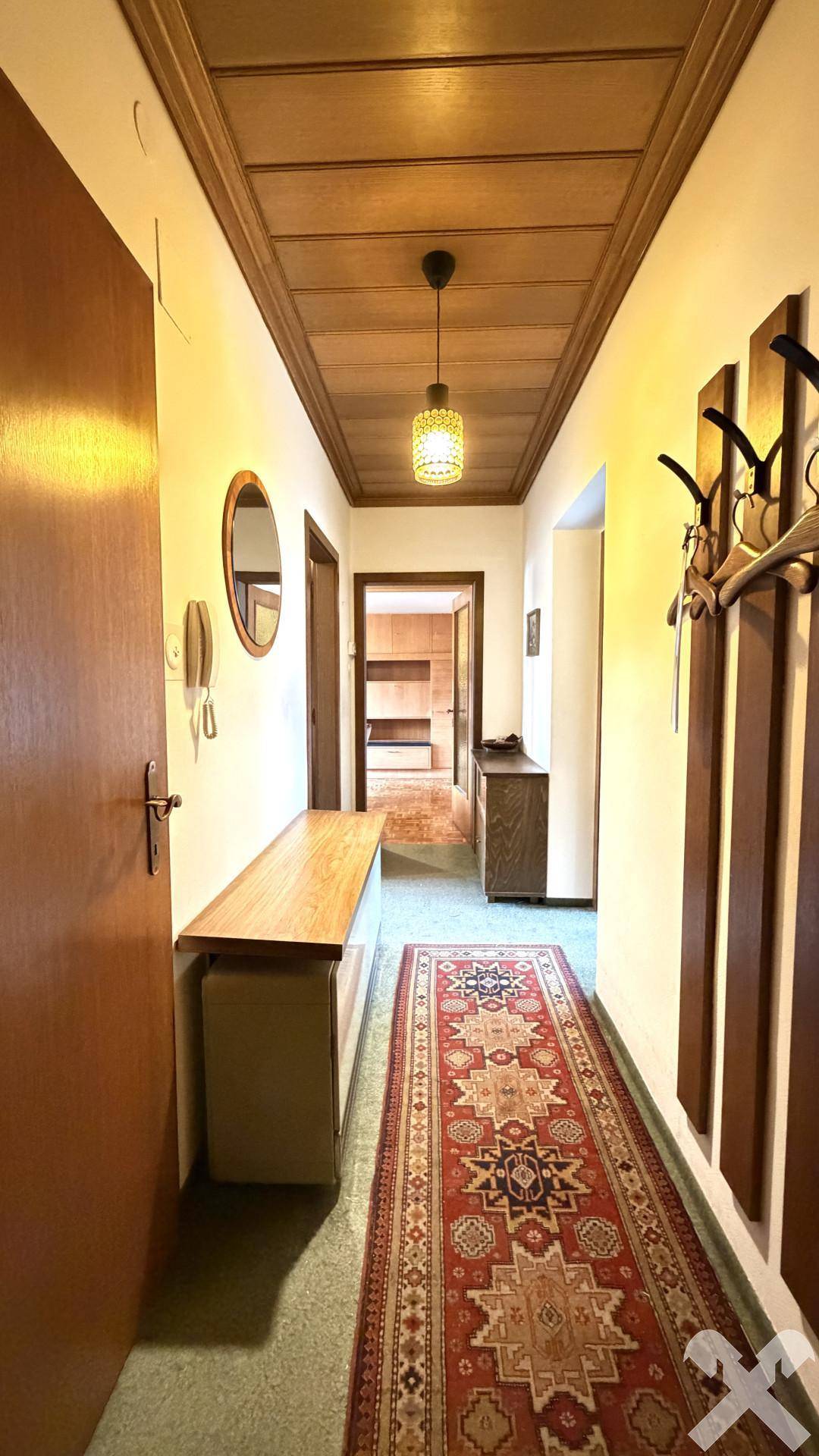 Langer Flur mit Holzdecke, Teppichläufer und Garderobe, führt zu weiteren Räumen.