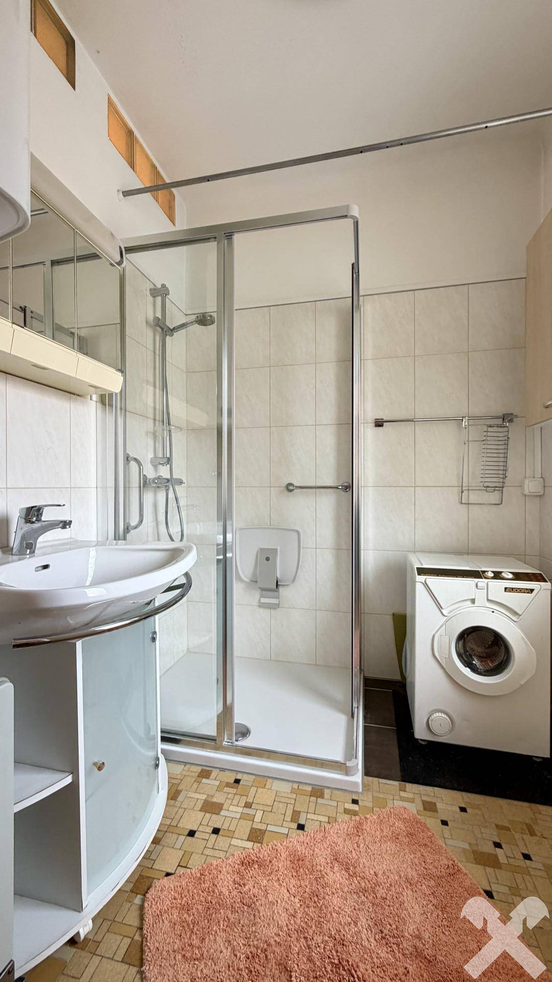 Badezimmer mit Duschkabine, Waschbecken und Waschmaschine, in hellem Fliesendesign.
