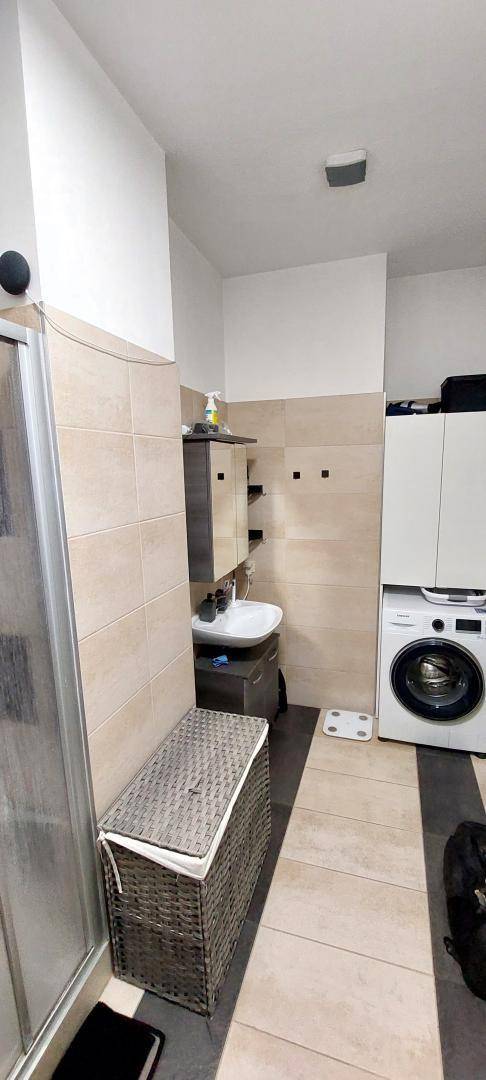 Badezimmer mit Waschmaschine, Einzelwaschbecken und Fliesenboden.