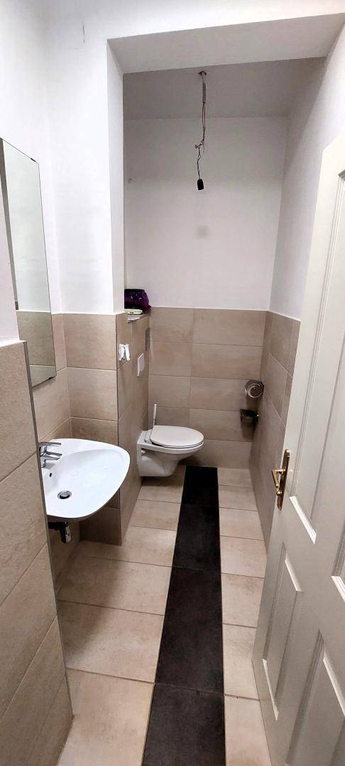 Separates WC mit wandhängender Toilette, Einzelwaschbecken und Fliesenboden.