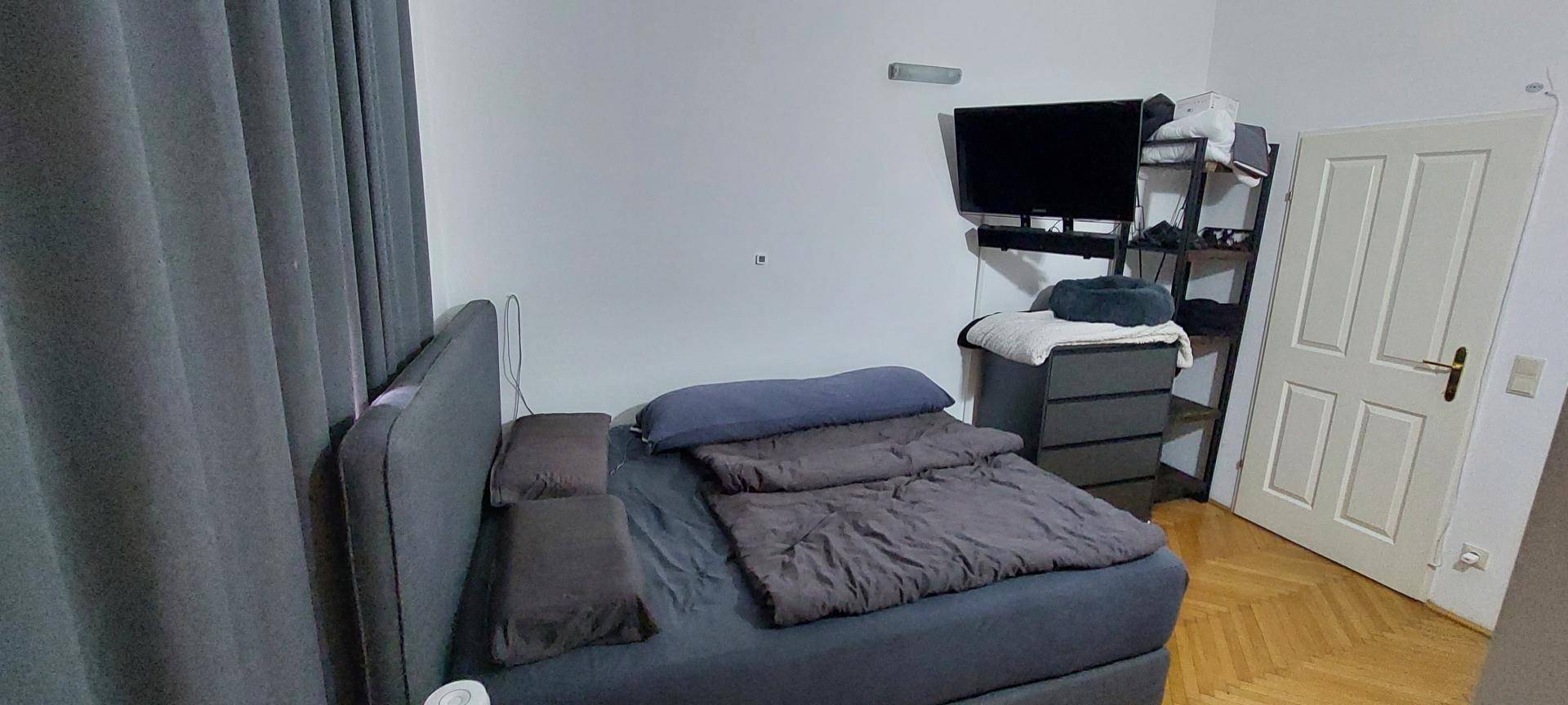 Schlafzimmer mit Doppelbett, Fernseher und Holzparkettboden.