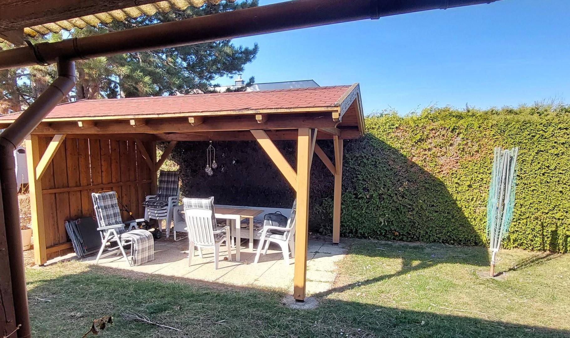 Überdachte Terrasse mit Gartenmöbeln und hoher Hecke im Hintergrund, ideal für Entspannung.