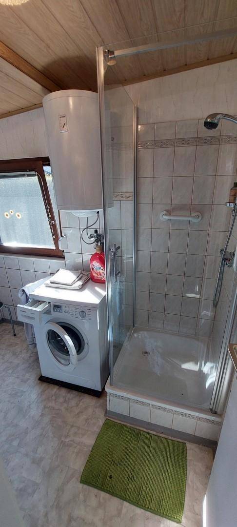 Kleines Badezimmer mit Duschkabine, Waschmaschine und Boiler, funktional eingerichtet.