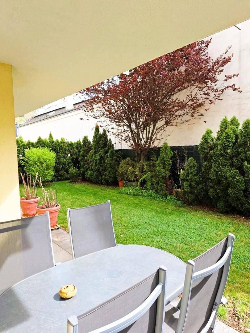 Gemütliche Terrasse mit Gartenmöbeln und Blick auf den grünen Garten mit Bäumen.