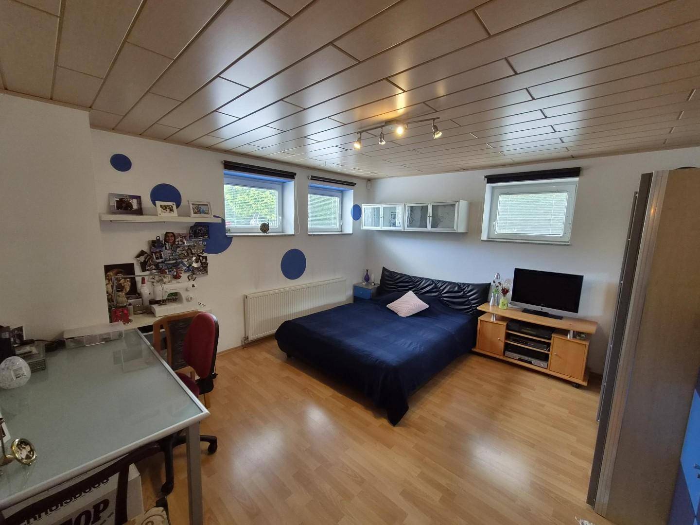 Gemütliches Schlafzimmer mit Holzboden, blauer Wanddekoration und zwei Fenstern.
