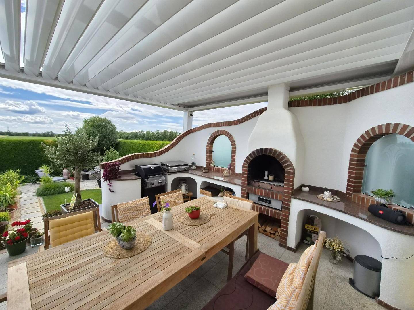 Überdachte Terrasse mit Außenküche, Grillbereich und großem Esstisch für gesellige Stunden.
