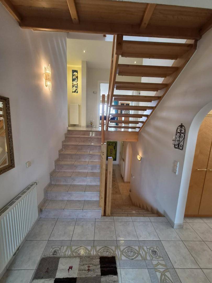Treppenhaus mit gefliestem Boden, Holztreppe und dekorativen Wandleuchten.