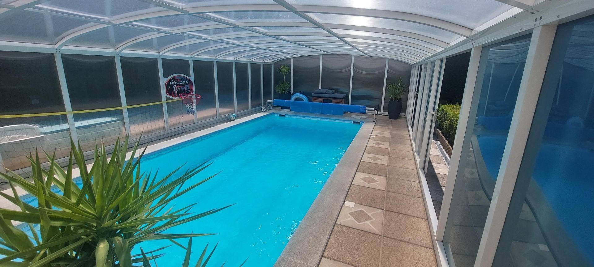 Überdachter Swimmingpool mit klarem Wasser, umgeben von einer transparenten Konstruktion.
