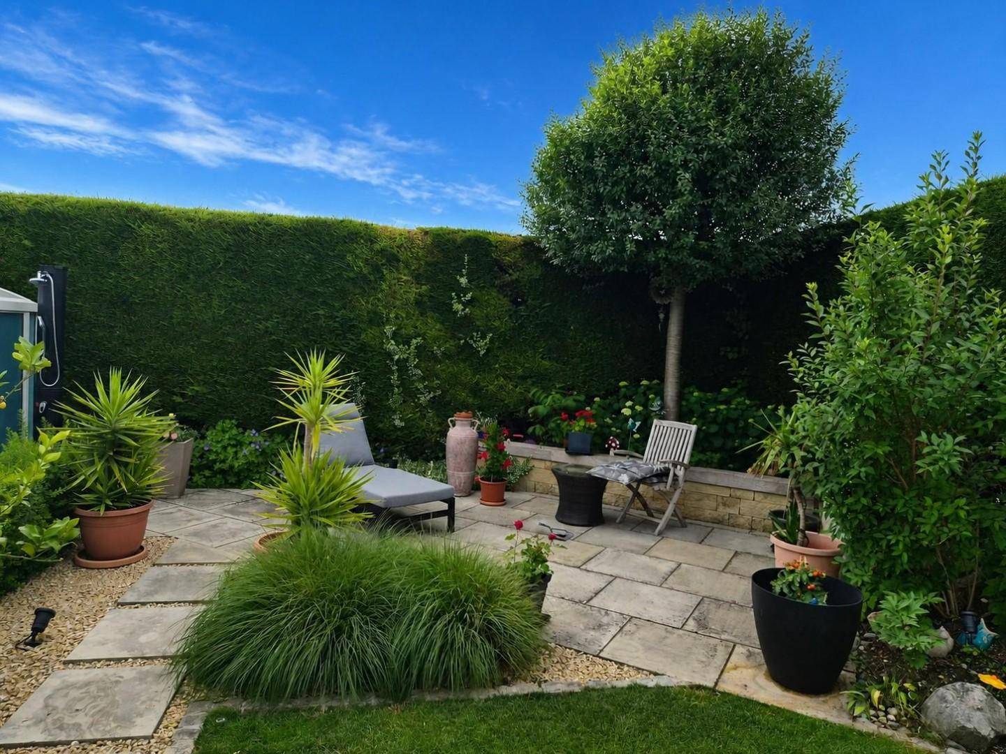 Gepflegter Gartenbereich mit Steinplatten, Rasenfläche und hohen Hecken für Privatsphäre.