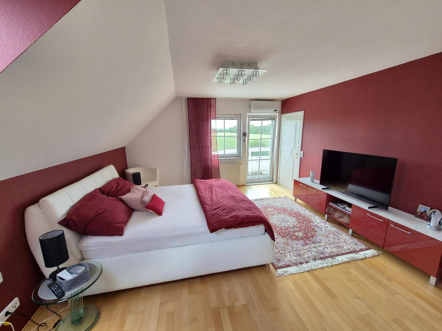 Schlafzimmer im Dachgeschoss mit roter Akzentwand, Holzboden und Balkonzugang.