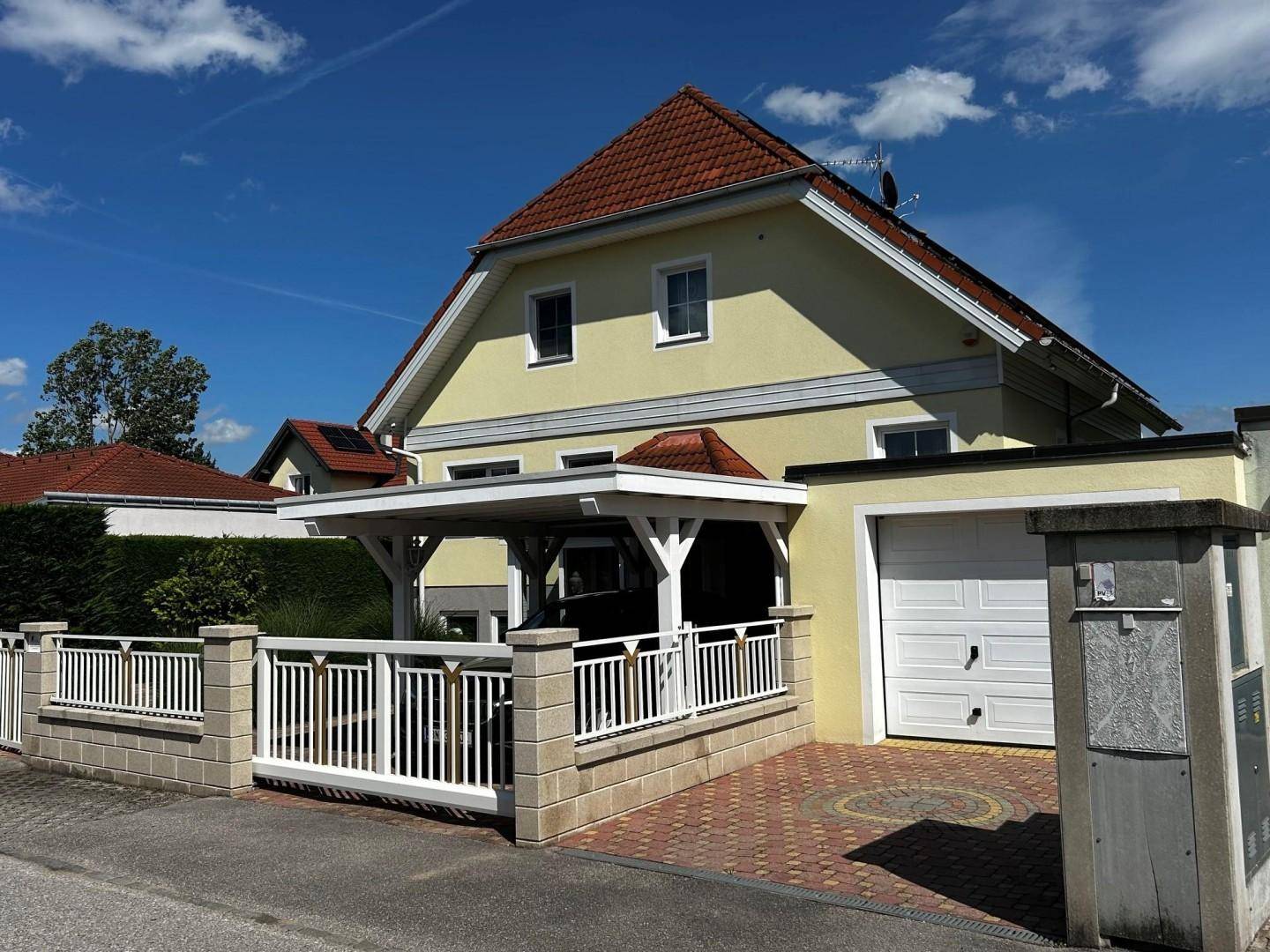 Ansicht des Hauses von der Straße mit Garage, Zaun und gepflasterter Einfahrt.