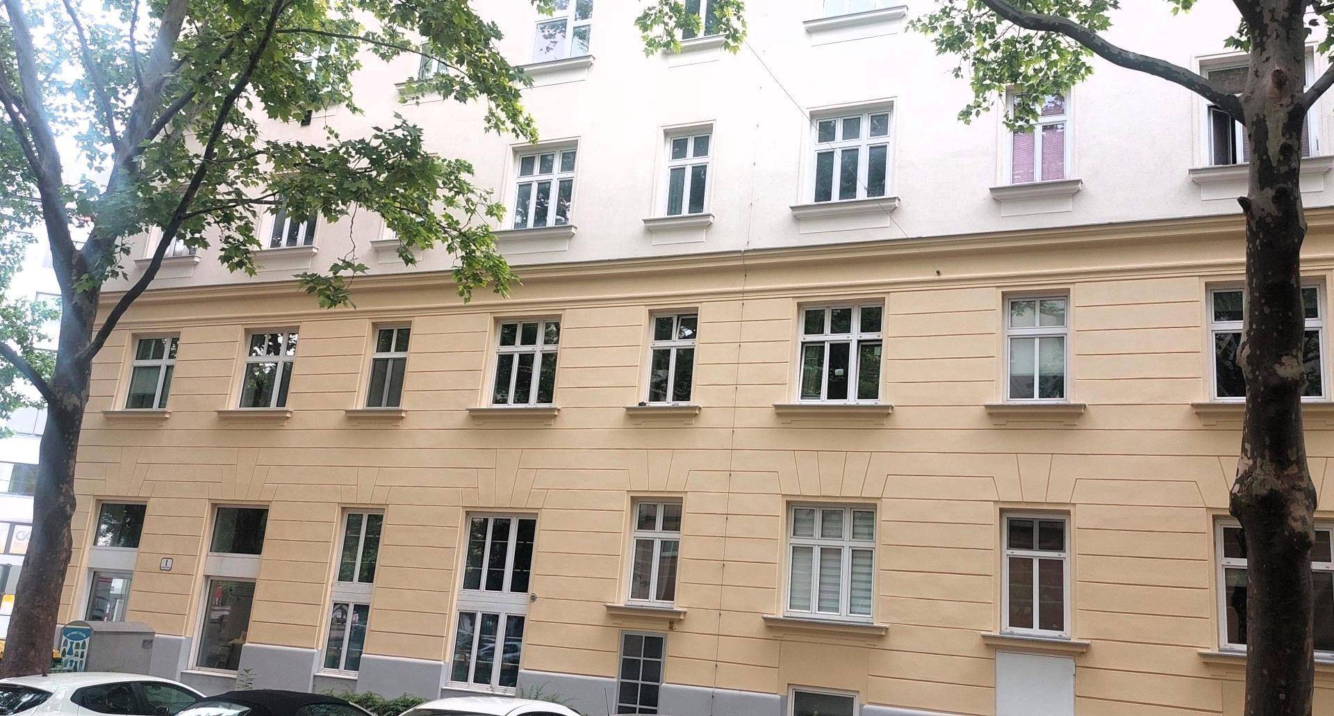 Seitenansicht eines mehrstöckigen Gebäudes mit zahlreichen Fenstern und Bäumen im Vordergrund.