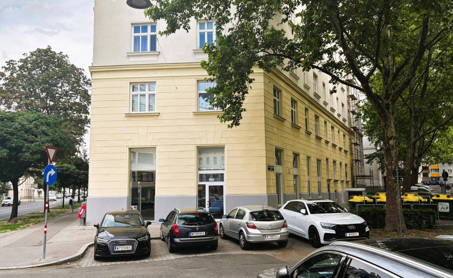 Gebäudeecke mit parkenden Autos und einem Verkehrsschild, typisch für eine städtische Lage.