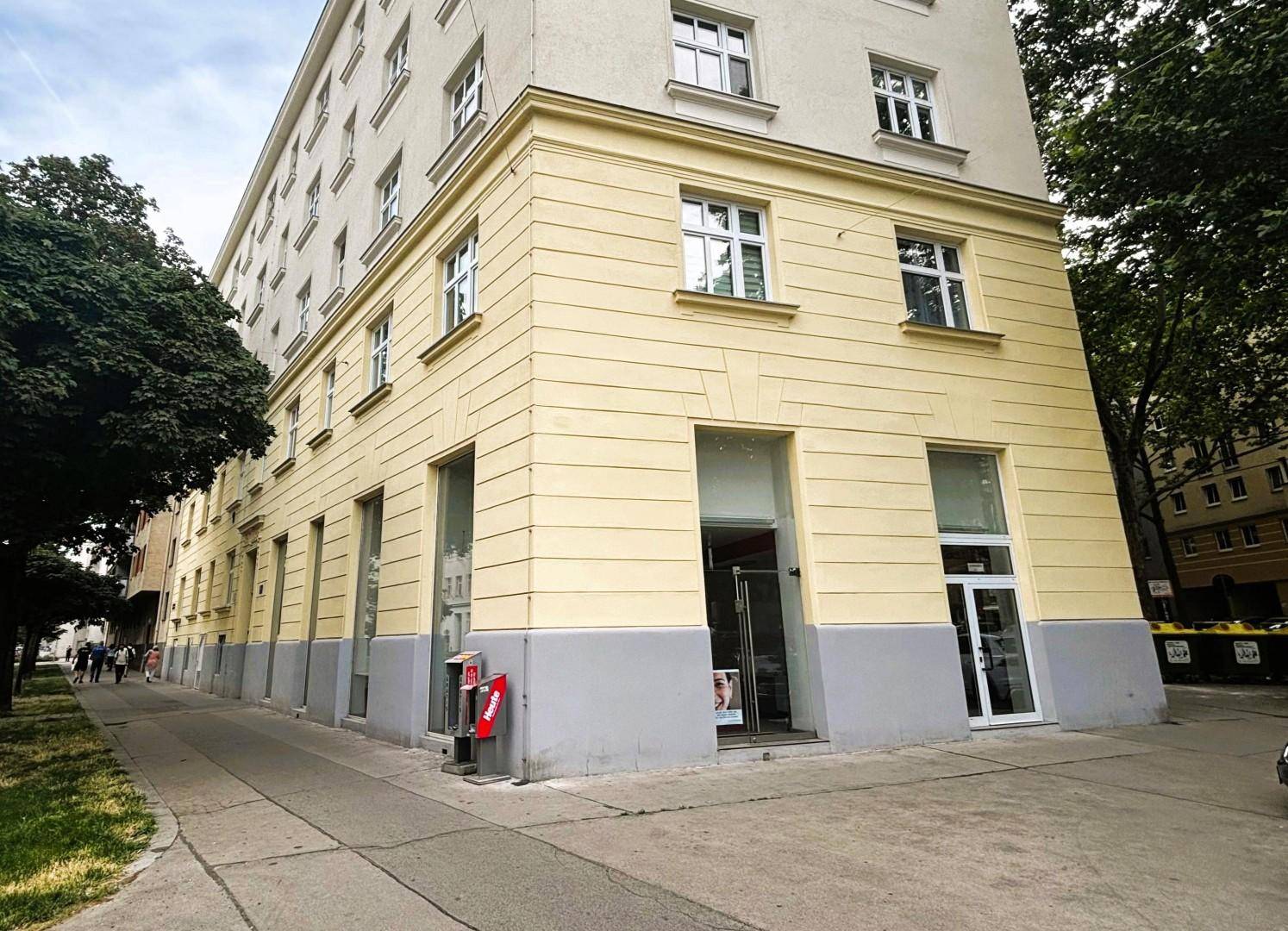 Ansicht der Gebäudefassade im Erdgeschoss mit großen Fenstern und einem Eingangsbereich.