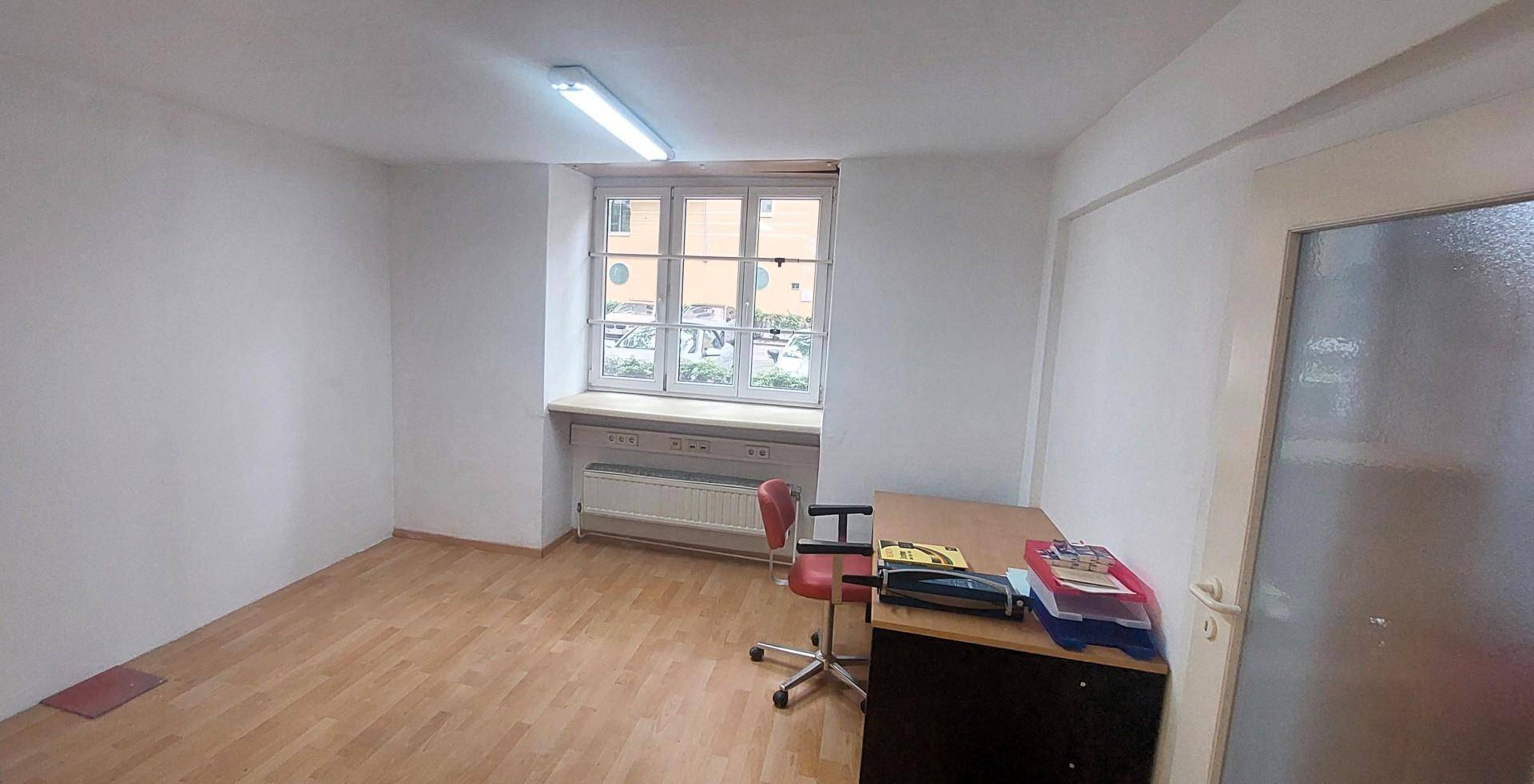 Kleines Büro mit Holzfußboden, einem Schreibtisch und einem Fenster mit Blick nach draußen.
