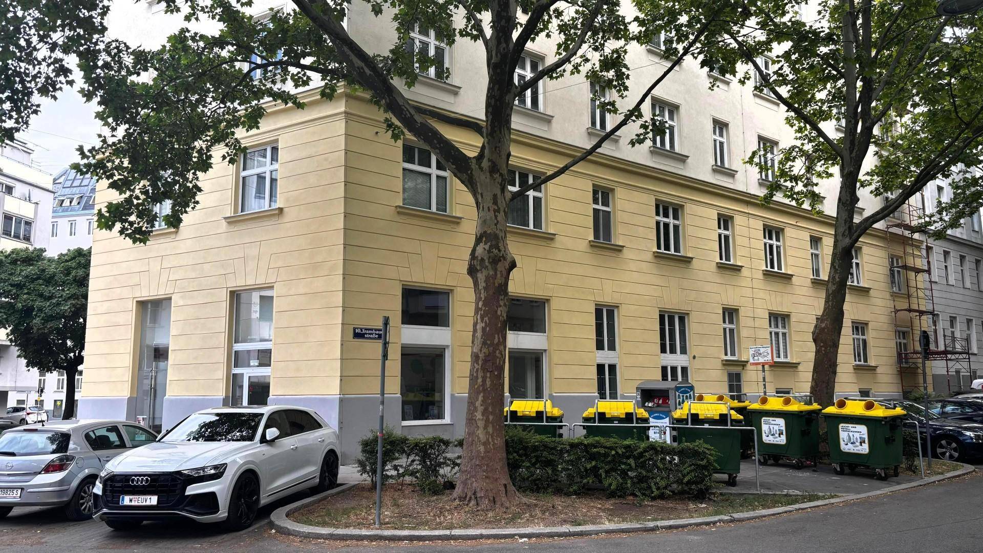 Gebäudeecke mit Bäumen und Müllcontainern, zeigt die städtische Umgebung des Anwesens.