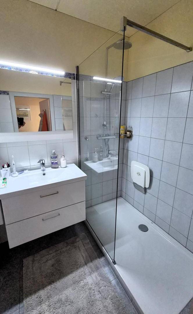 Modernes Badezimmer mit begehbarer Dusche, Waschbecken und hellen Fliesen an den Wänden.