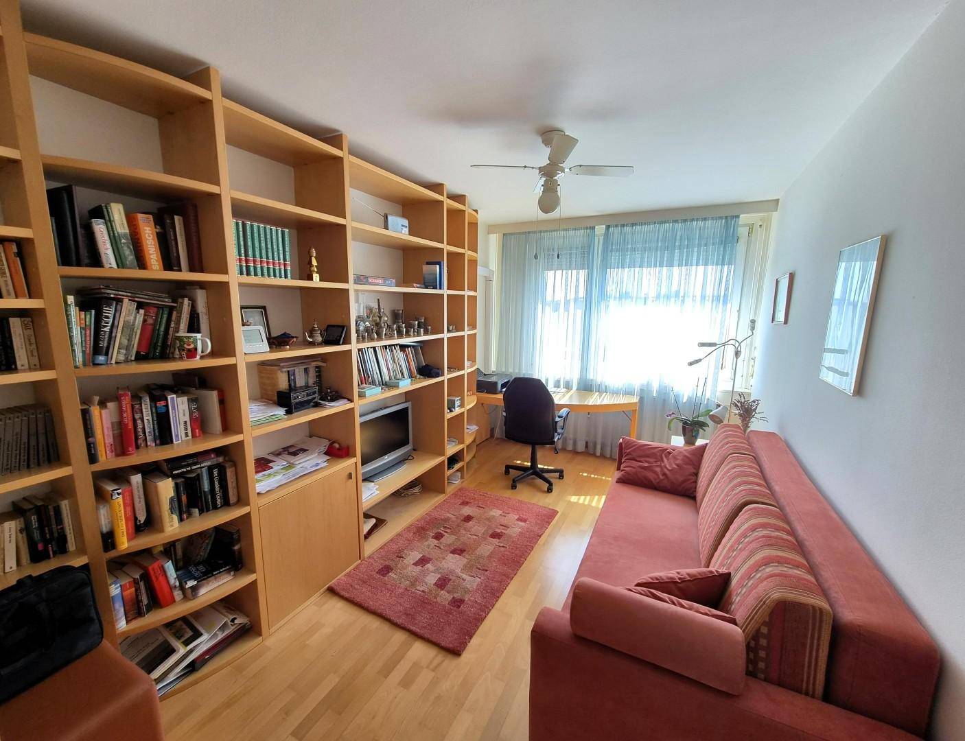 Arbeitszimmer mit Bücherregalen, Sofa und großem Fenster, ideal für Home-Office oder Gäste.