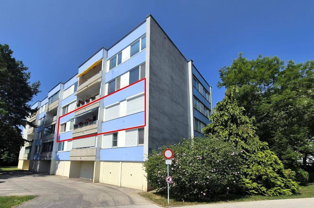 Seitenansicht des Mehrfamilienhauses mit blauer Fassade und mehreren Balkonen unter klarem Himmel.