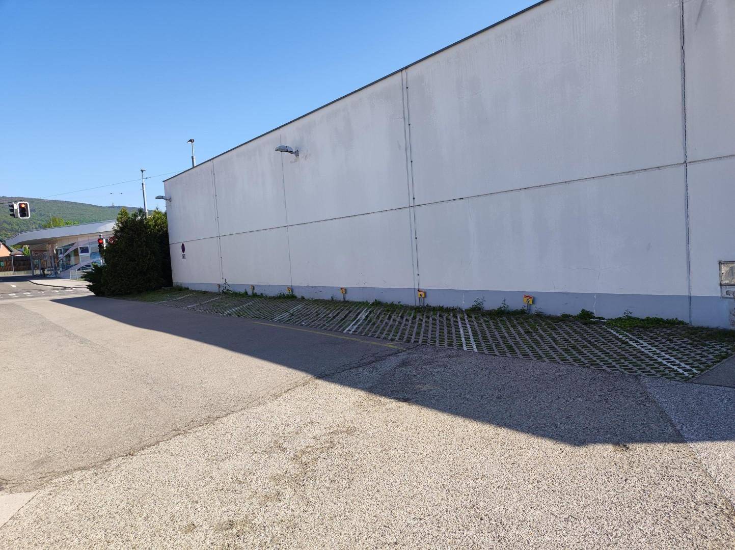 Seitenansicht des Gebäudes mit einer großen, weißen Wandfläche und einem Parkplatz mit Rasengittersteinen im Vordergrund.