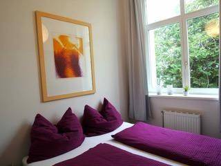 Gemütliches Schlafzimmer mit lila Bettwäsche und großem Fenster mit Blick ins Grüne.