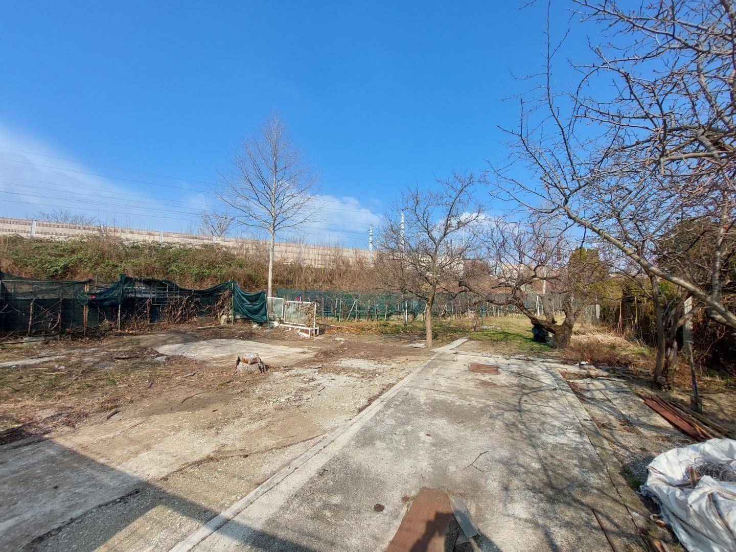 Weitläufiger Gartenbereich mit kahlen Bäumen, Betonflächen und Blick auf die Umgebung.