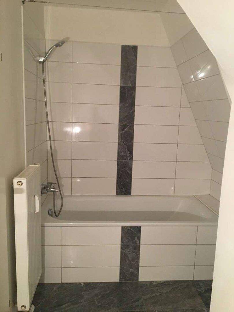 Badezimmer mit Badewanne und Dachschräge, gefliest in Weiß und Grau.