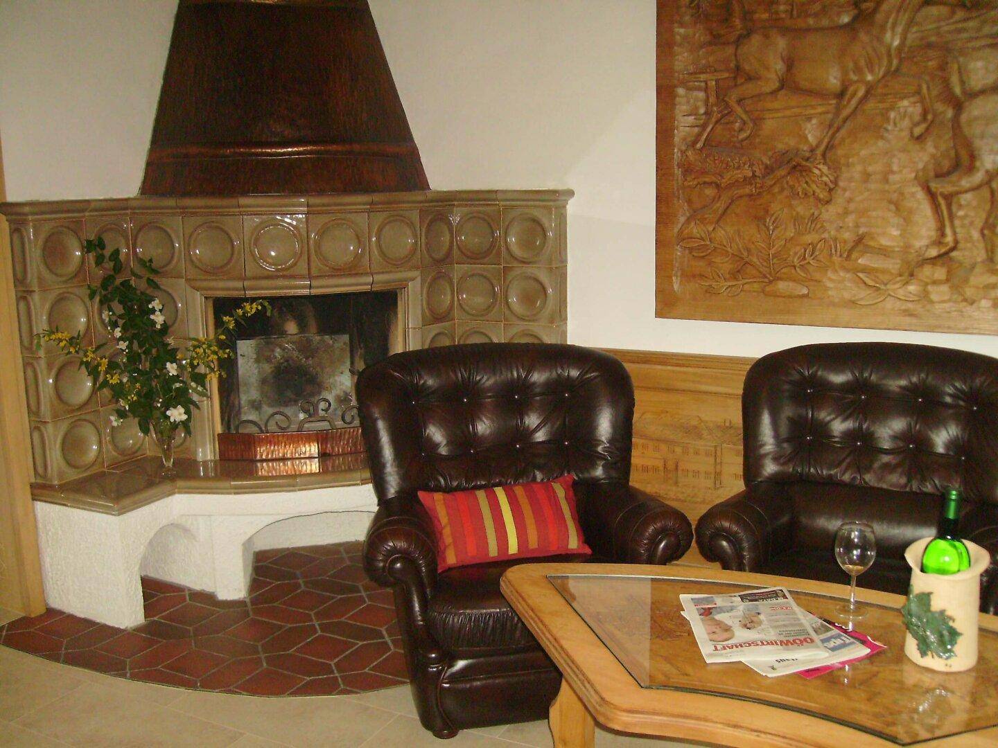 Wohnzimmer mit großem Kachelofen, zwei Ledersesseln und Holztisch.