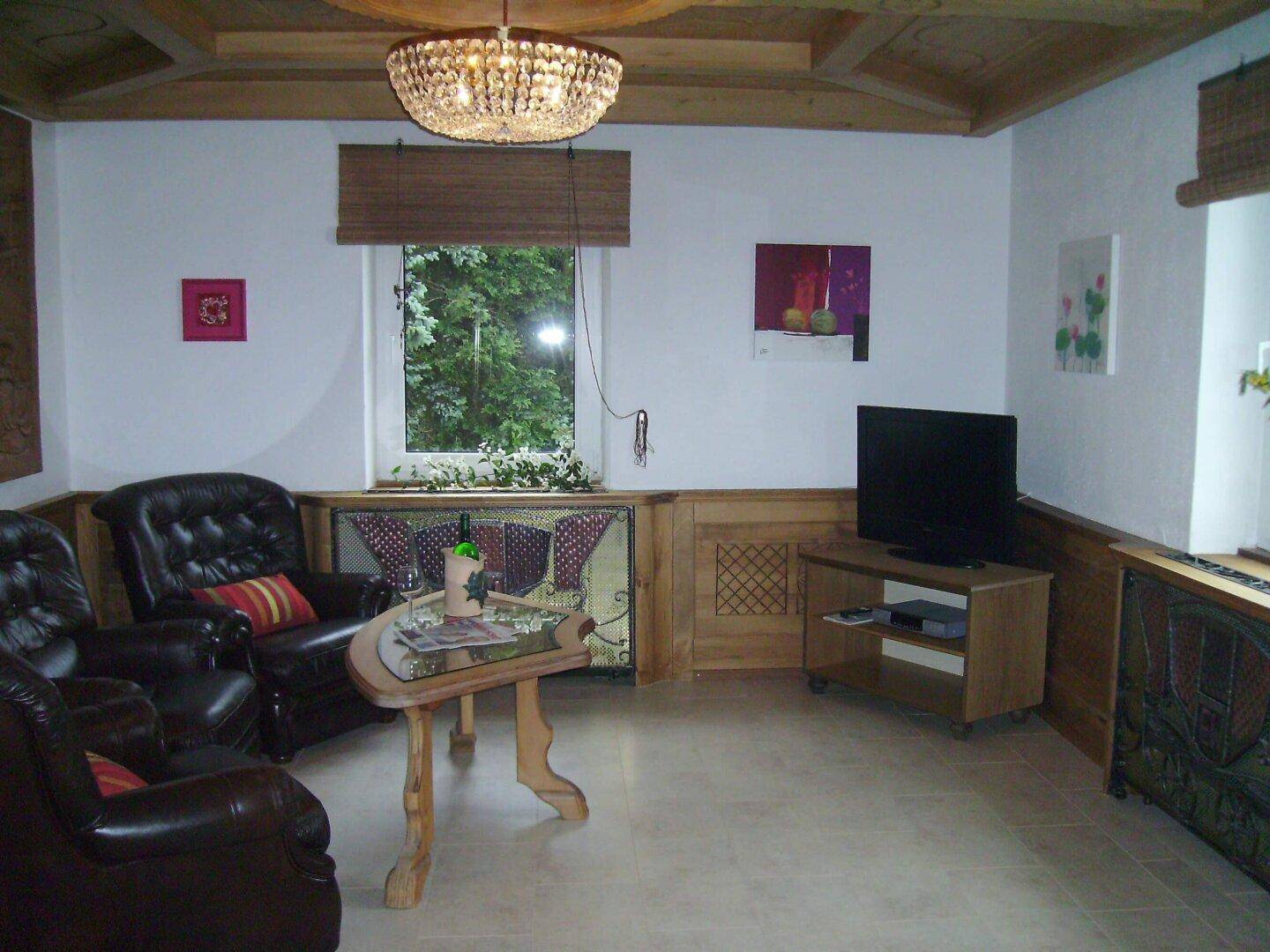 Wohnzimmer mit Kronleuchter, Holztäfelung und Decke mit Holzbalken.