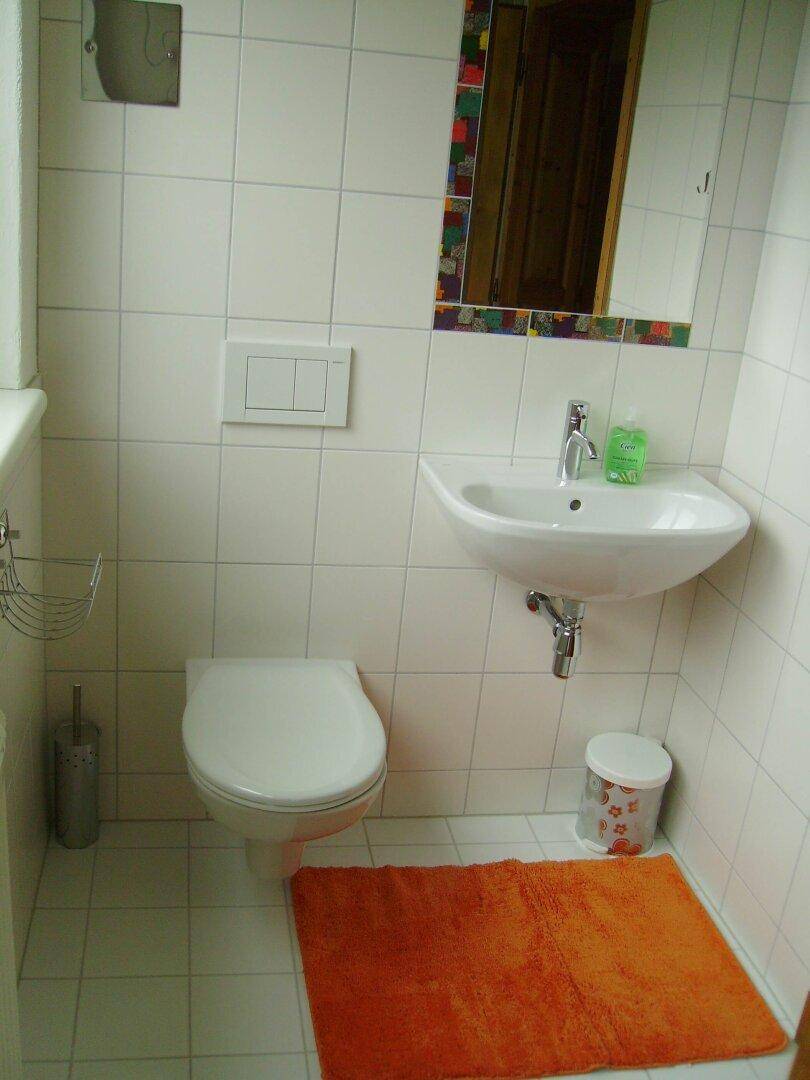 Helles Badezimmer mit weißen Fliesen, Wand-WC und Waschbecken.