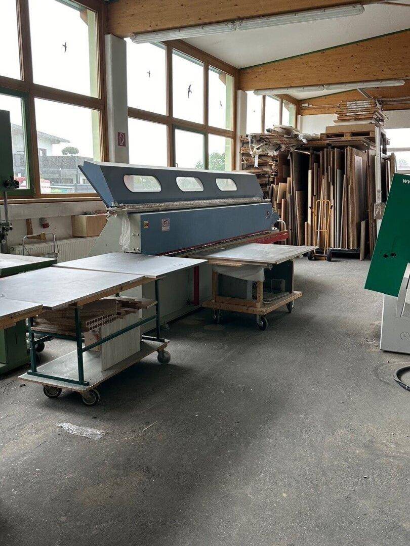 Geräumige Werkstatt mit Holzbearbeitungsmaschinen, großen Fenstern und gelagerten Holzplatten.