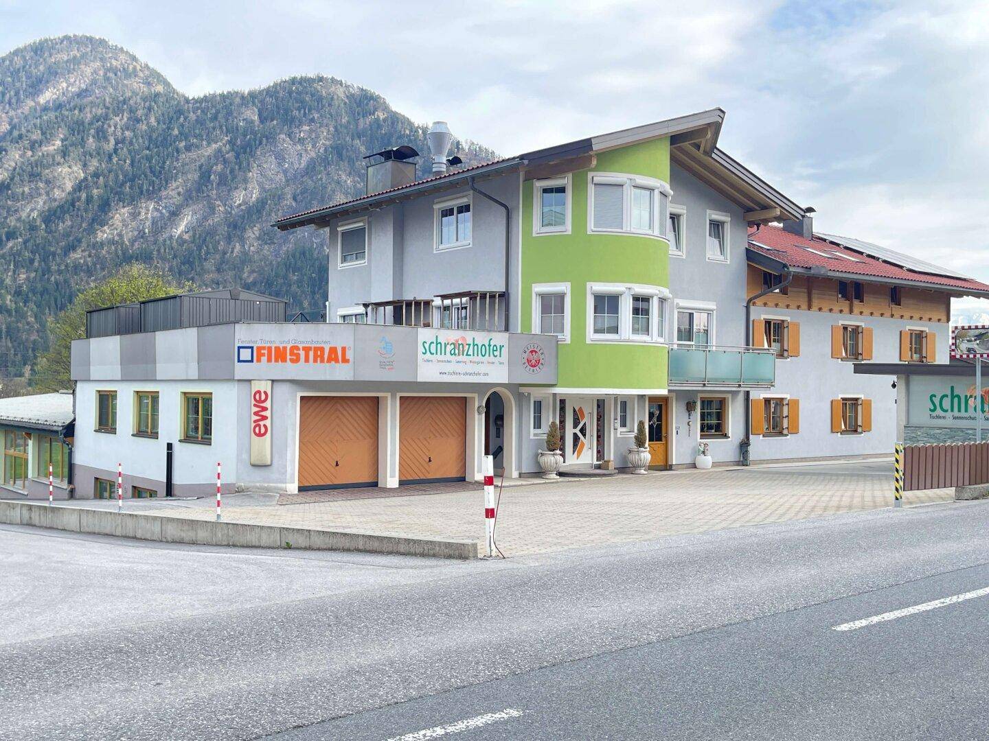 Gewerbegebäude mit farbiger Fassade und Garagentoren an einer Straße, umgeben von Bergen.