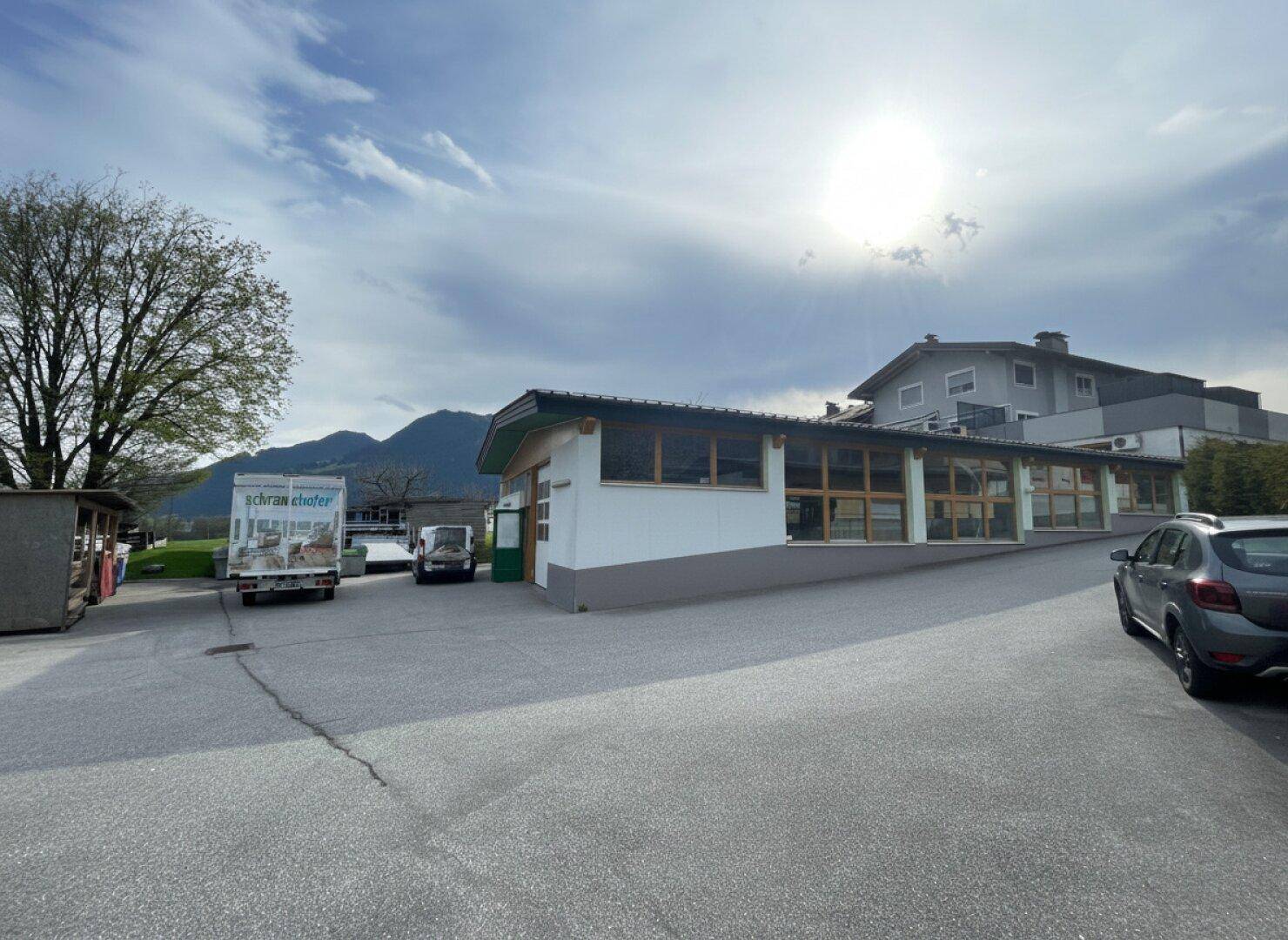 Weitläufiger Außenbereich eines Gewerbegebäudes mit Lieferwagen und Bergen im Hintergrund bei Sonnenschein.