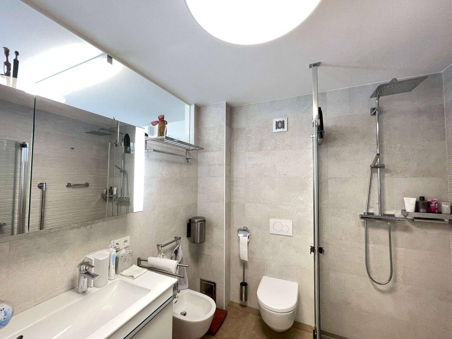 Zeitgemäßes Badezimmer mit ebenerdiger Dusche, Wand-WC und Bidet, ausgestattet mit modernen Armaturen.