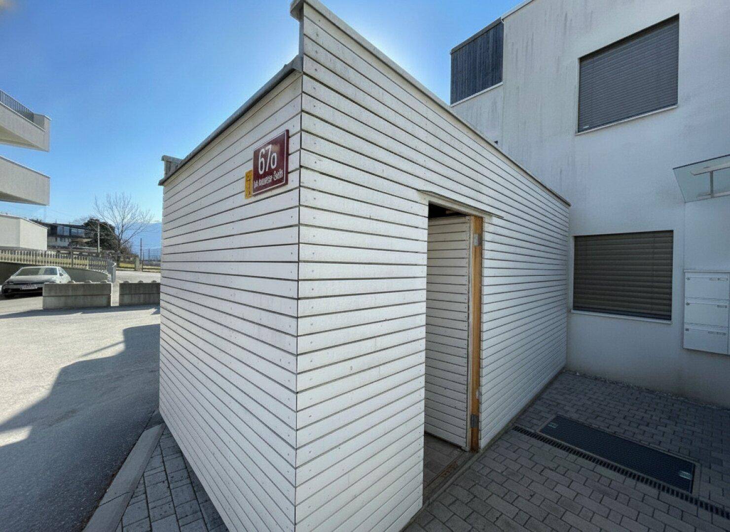 Kleines Nebengebäude mit Holzverkleidung und Hausnummer, Teil eines modernen Wohnkomplexes.