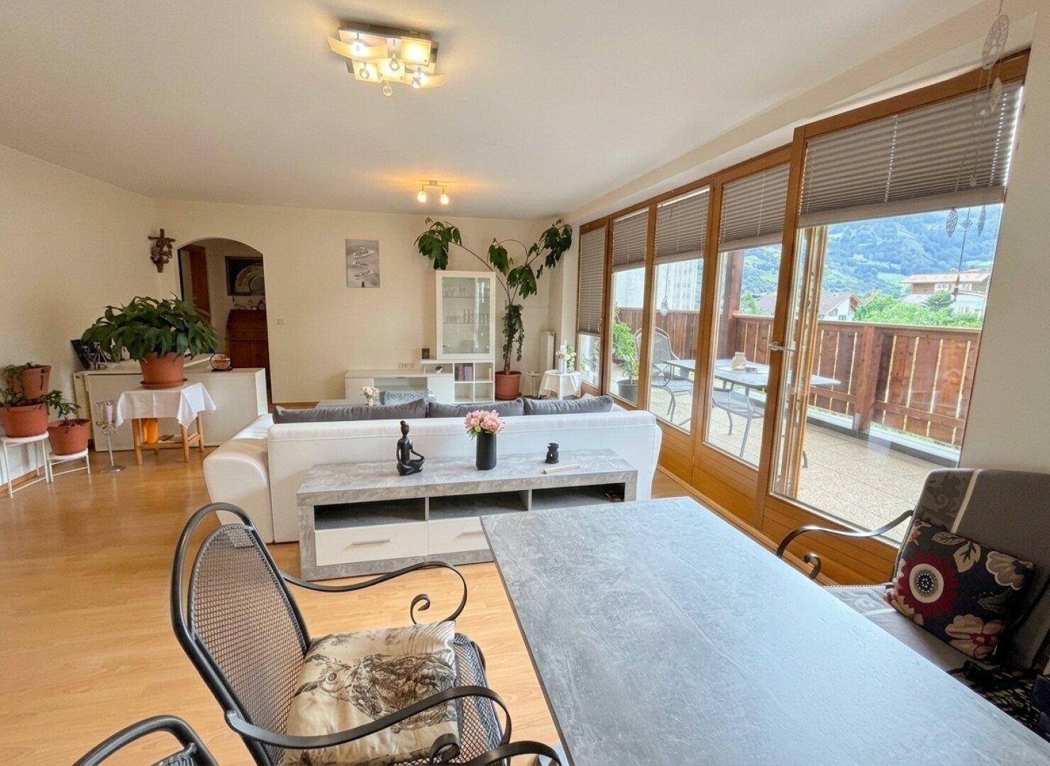 Gemütlicher Wohnbereich mit Holzboden, großem Fenster und Blick auf die umliegende Landschaft.
