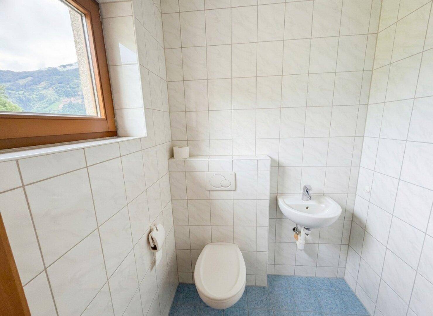 Kleines Gäste-WC mit weißer Fliesenwand, Waschbecken und Fenster.
