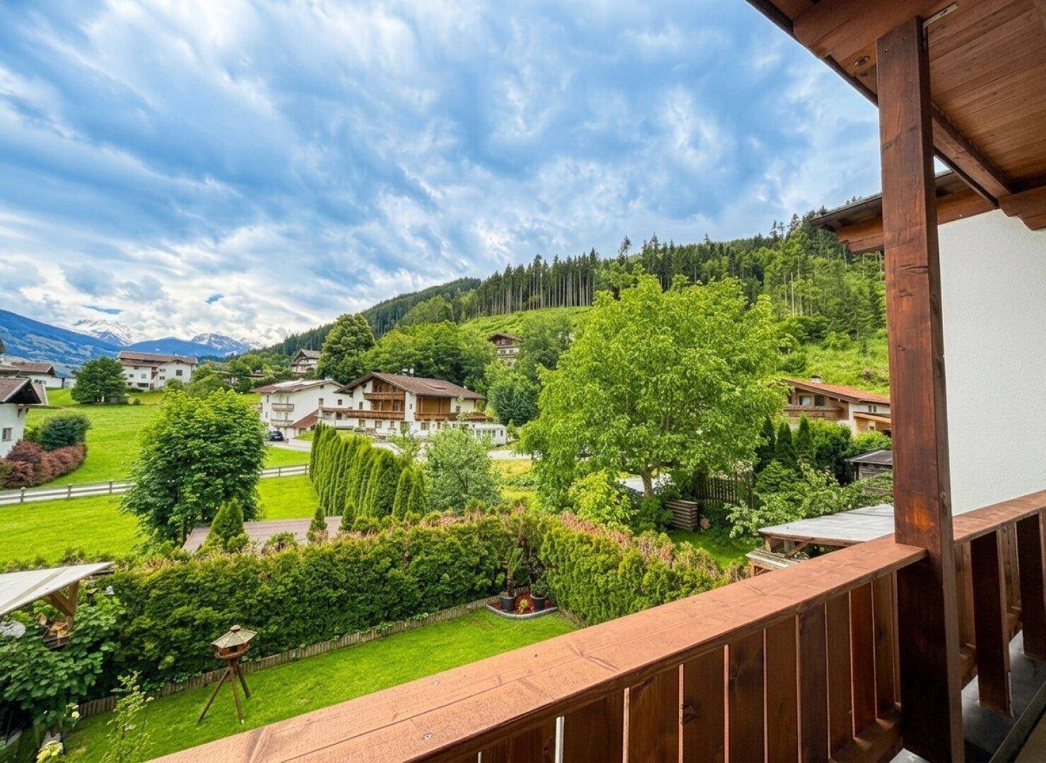 Balkon mit weitem Blick über grüne Wiesen, Bäume und die umliegende Berglandschaft.