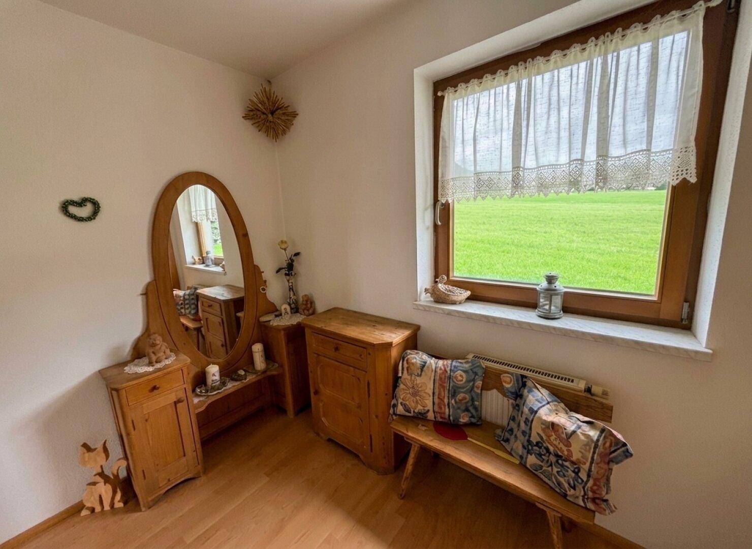 Schlafzimmer mit traditionellen Holzmöbeln, Holzboden und Fenster mit Blick ins Grüne.
