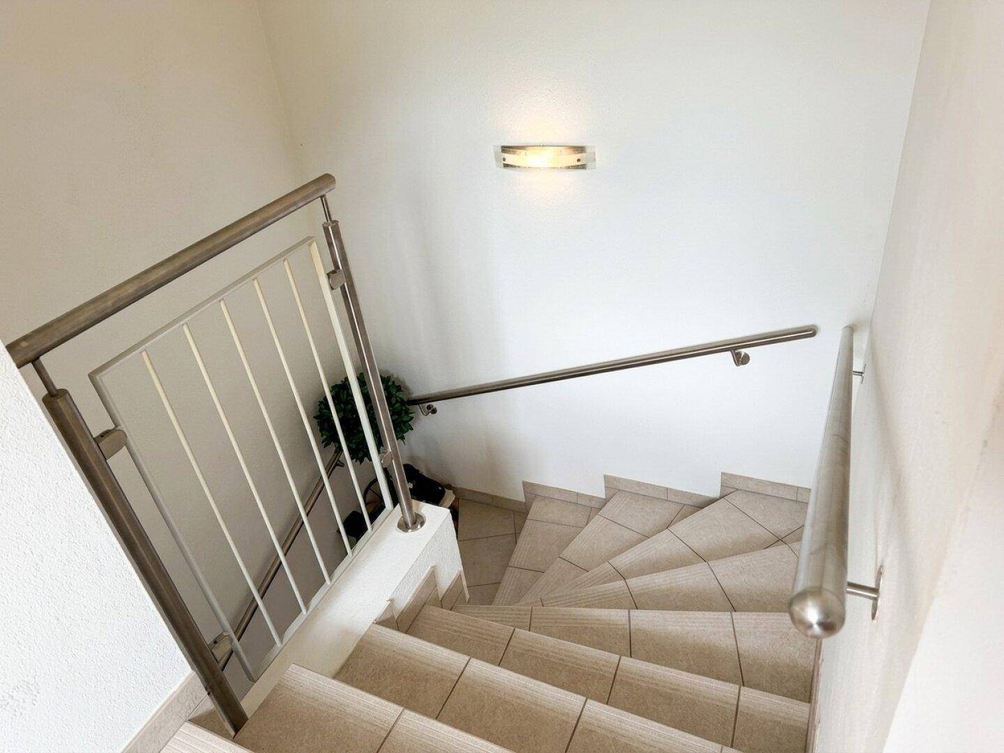 Treppenhaus mit gefliesten Stufen und modernem Edelstahlgeländer.