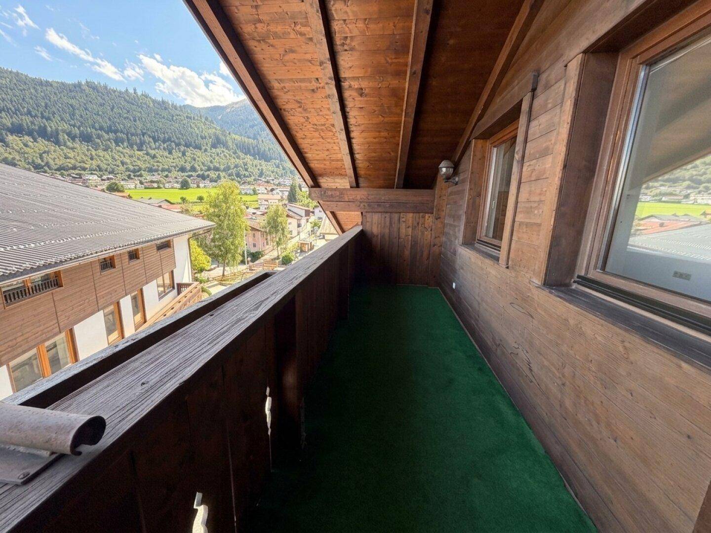 Schmaler Holzbalkon mit Kunstrasenboden und Panoramablick auf die grüne Berglandschaft.
