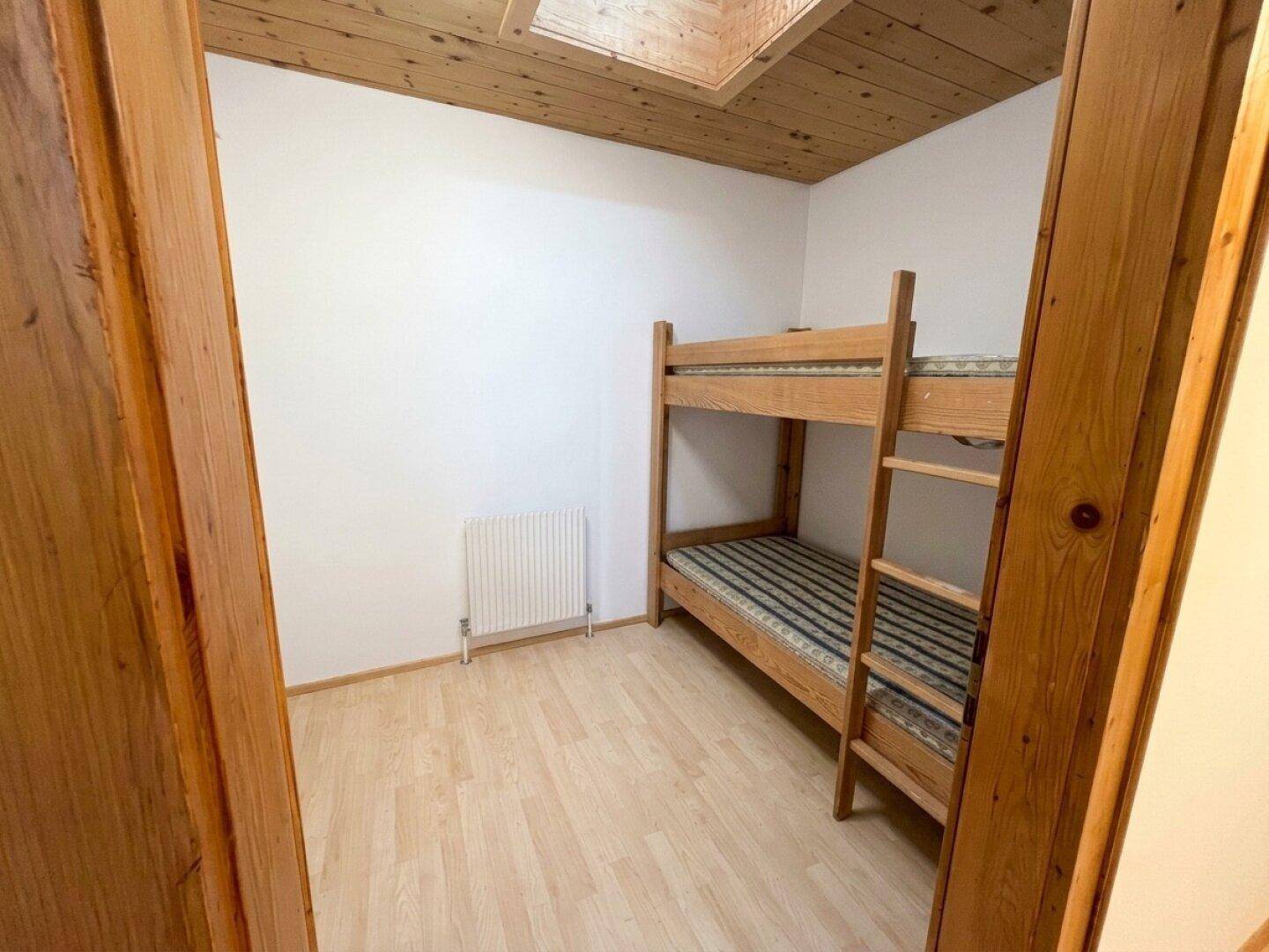 Kleines Schlafzimmer mit Etagenbett, hellem Laminatboden und Holzdecke.