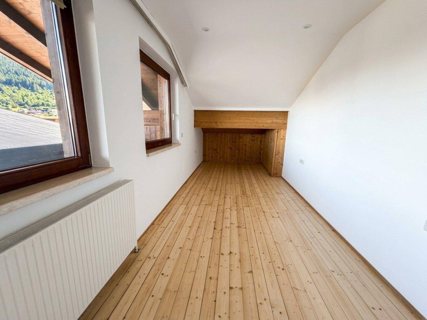 Heller Raum mit Holzplankenboden, schrägen Wänden und Fenstern für viel Tageslicht.