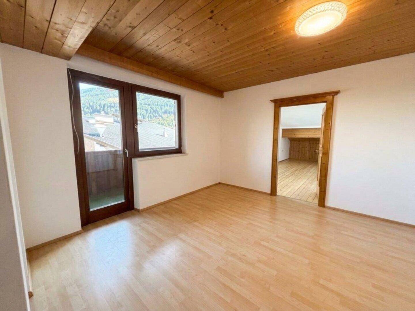 Heller Raum mit Laminatboden, Holzdecke und Zugang zu einem Außenbereich.