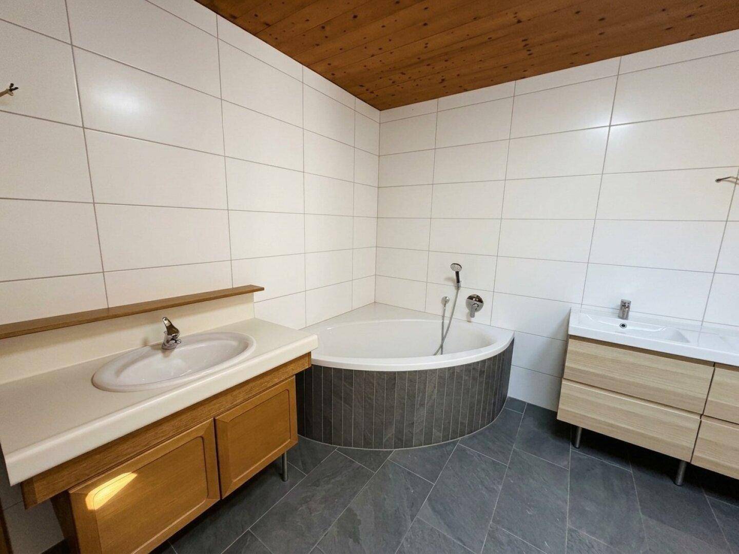 Modernes Badezimmer mit weißen Wandfliesen, dunklem Boden und einer Eckbadewanne.