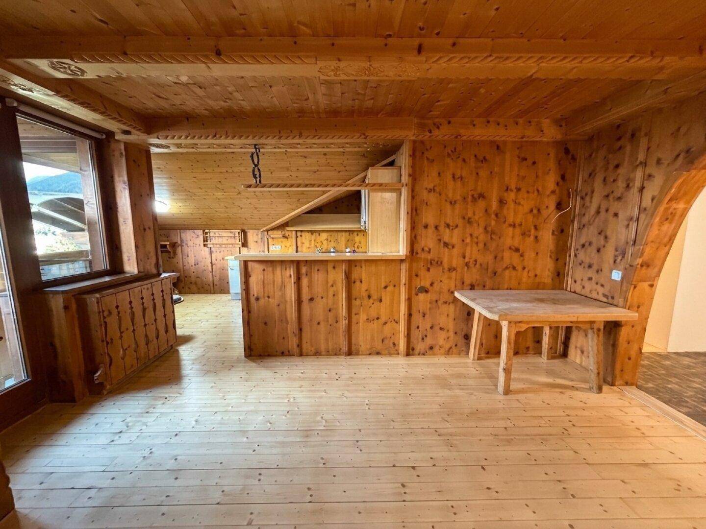 Rustikaler Wohnbereich im Dachgeschoss mit Holzboden, Holzvertäfelung und kleiner Küchenzeile.