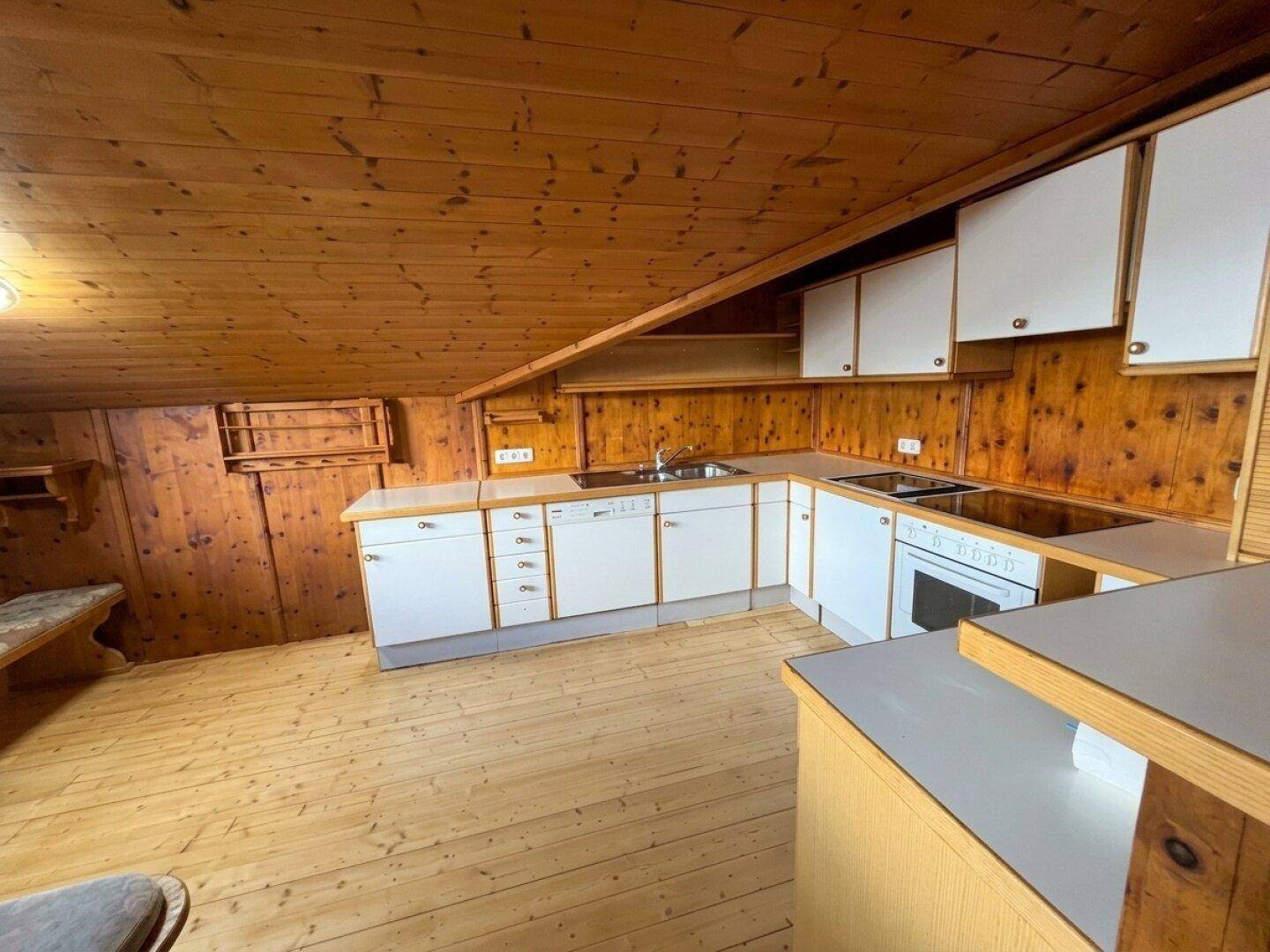 Funktionale Küche mit weißen Schränken, Kochfeld und Holzvertäfelung im Dachgeschoss.