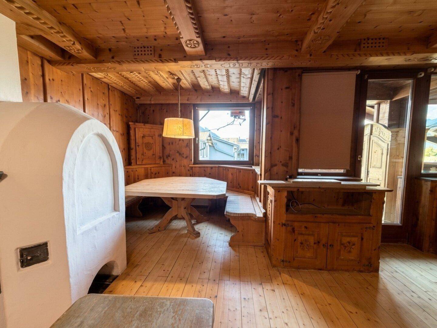 Gemütlicher Essbereich im alpinen Stil mit Kachelofen, Holztisch und eingebauten Sitzbänken.